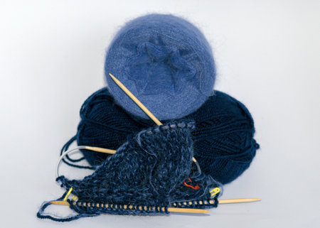 photo with knitting needles, balls of yarn and a piece of knitted jacket on a solid white...