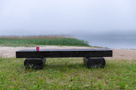 mystical fog picture, lake view with white fog, wooden bench in foreground, blurred misty lake backgroundの写真素材