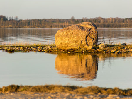 landscape with a lonely stone on the lake shore, calm lake water and sky reflectionの写真素材