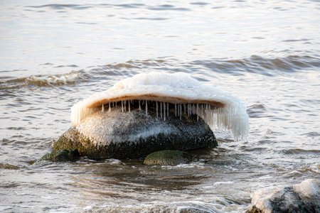 colorful winter landscape by the sea, frozen stones with icicles on the seashore, sunset colors, snow and iceの写真素材