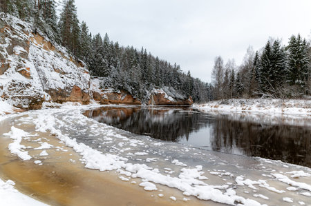 winter landscape with river and sandstone outcrops, river frozen with ice, snow fallen on trees,...