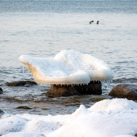 colorful winter landscape by the sea, frozen stones with icicles on the seashore, sunset colors,...