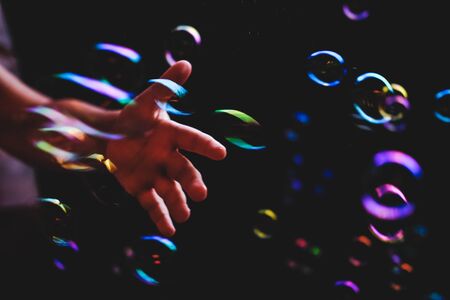Hand trying to catch colorful bubbles over dark backgroundの写真素材