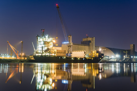 unloading cargo ship with containers in sea port at night