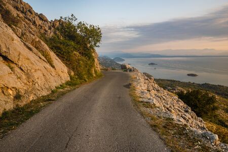 a narrow, winding road that runs on the edge of a cliff above Lake Skadar in Montenegro