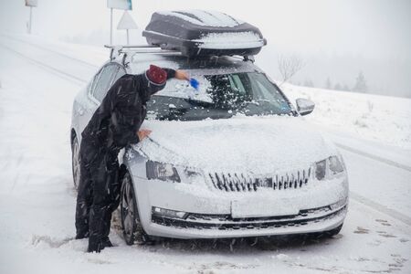 driver clearing the car during snow blizzard in the mountainsの写真素材