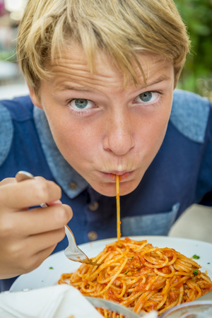 blond boy with blue eyes eating spaghettiの写真素材