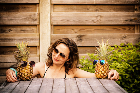 woman between two pineapples wearing sunglasses, as if she's between her best friendsの写真素材