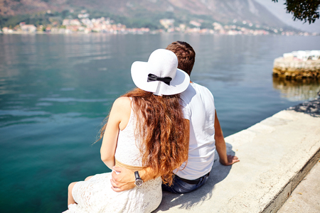 Cute couple in love sitting on a concrete pier on a blue background of the sea. Young man and woman hugging. Summer sunny dayの写真素材