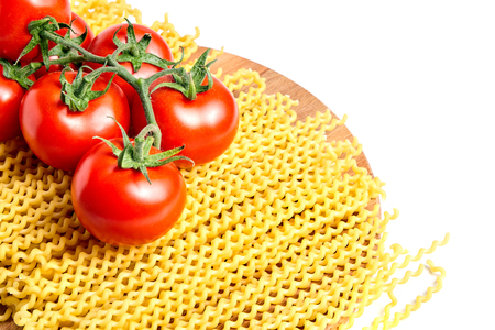 Heap fusilli bucati lunghi italian pasta and Fresh Red ripe tomatoes on a green branch laying on wooden beech board. Isolated on white backgroundの写真素材