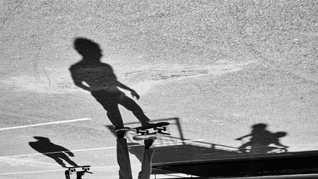 Shadow of skateboarders and bicycler on asphalt. Black and white image