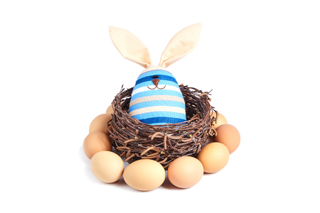 A soft toy of a striped rabbit, sitting in a basket of birch branches.の写真素材