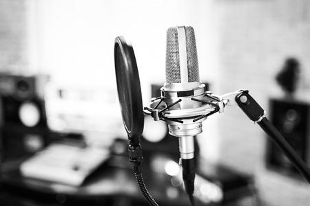 Silver condenser microphone with pop filter and anti-vibration mount. Music studio. Professional sound and voice recording instrument. Side view. Selective focus. Blurred background. Black and whiteの写真素材