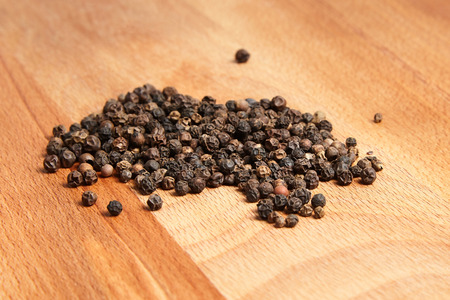 Heap of black peppercorns on  wooden beech cutting board backgroundの写真素材