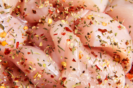 Uncooked poultry meat with spices. Sliced pieces of raw chicken fillet sprinkled with various dry seasoningsの写真素材