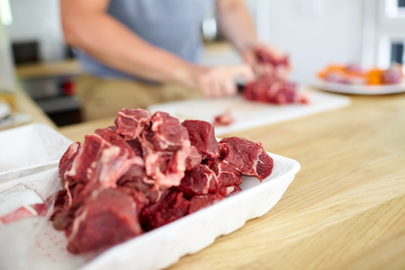 Cooking. Pieces of red chopped meat in a white plastic tray. Second plan: men's hands chef. Selective focus. Blurred backgroundの写真素材