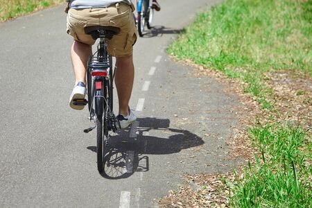 Adult man riding a bicycle. Cyclist in beige shorts. View from the back. Bike ride in the nature on a sunny summer dayの写真素材