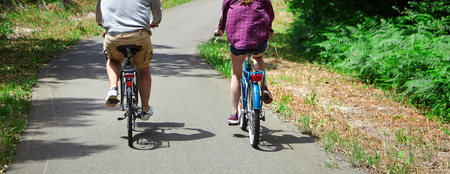 Loving married couple riding on bicycles. A man in beige shorts and a woman in a purple shirt. View from the back. Bike ride in the nature on a sunny summer dayの写真素材