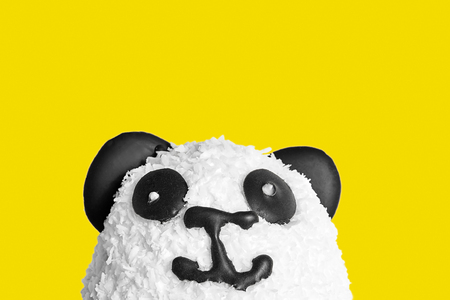 Sweet cake in the form of a panda head. Eyes, ears and nose made of dark chocolate. Sprinkled with coconut chips. Isolated on yellow backgroudの写真素材