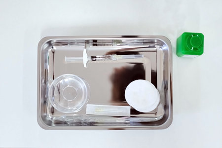 A new syringe filled with a medical product and lying on a silver tray. Tools for the procedure of...