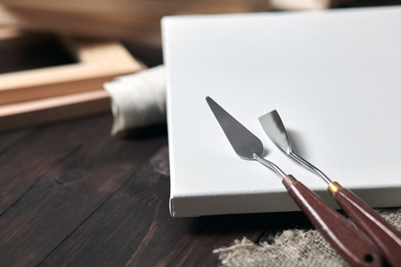 Artist tools: Palette knives lying on a white primed cotton canvas. wooden stretchers in the blurred background. Selective focusの写真素材