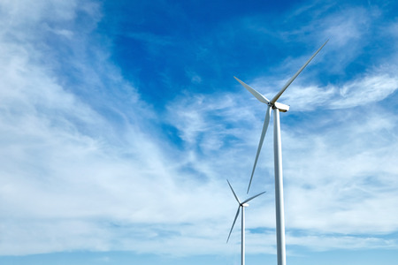 Two wind power turbines against a blue sky with white clouds. Renewable energy source. Powerful and ecological energy concept.の写真素材