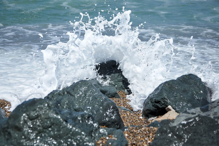 Sea wave crashing against a black stone with foam and splashes. Ocean shore. Rocky beach