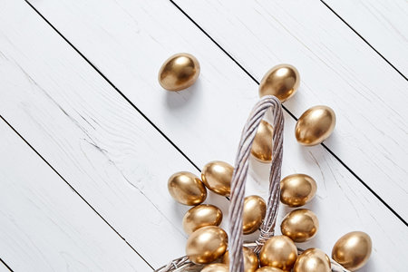 Easter golden eggs spilled out of wicker basket on white wooden table background. Top viewの写真素材