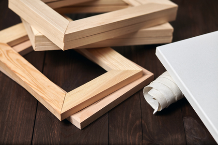 Wooden stretcher bars and a rolled canvas lying on a dark brown background, timber, subframesの写真素材