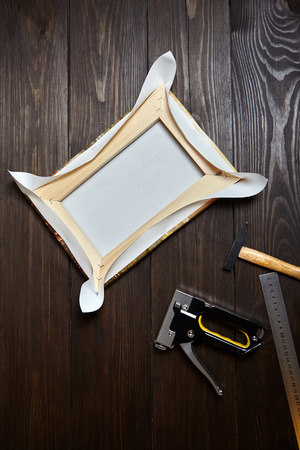 Canvas stretching on wood stretcher bar. Photo printed on canvas (back view),  hammer, steel ruler and stapler on brown wooden table, top viewの写真素材