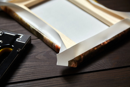 Canvas stretching on wood stretcher bar. Photo printed on canvas (back view) and stapler on brown wooden tableの写真素材