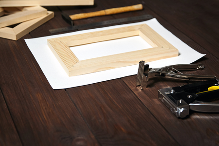 Stretching cotton canvas on wooden stretcher bar, stapler and canvas pliers on a brown tableの写真素材