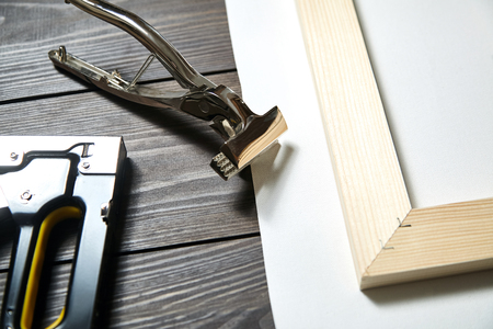 Stretching canvas on wooden stretcher bar, staple gun and canvas pliers on a brown tableの写真素材