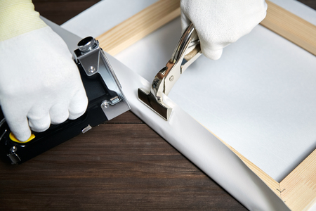 Canvas stretching. Wooden stretcher bar, staple gun, canvas pliers, male hand in white protect glovesの写真素材