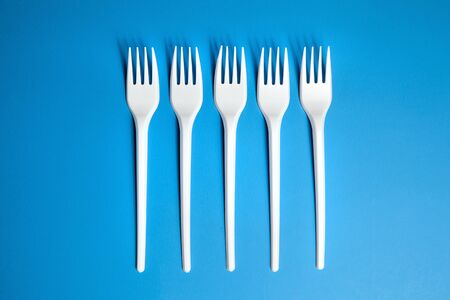 A row of lying white forks on blue background, top view. Disposable plastic tablewareの写真素材