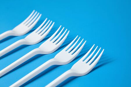A row of lying white forks on blue background. Disposable plastic tablewareの写真素材