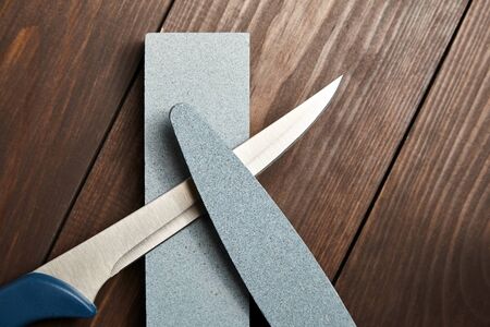 Whetstones and steel knife blade. Grindstones. Oval and rectangular double layer sharpening stone on wooden table backgroundの写真素材