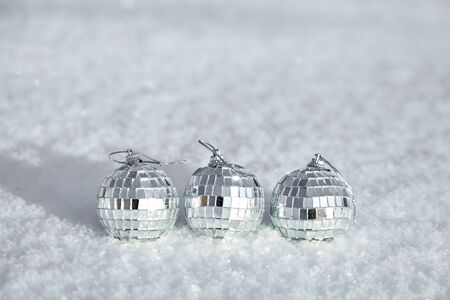Three toy mirror disco balls lie on the natural snow. Winter Christmas and New Year background. Frosty weather with loose snowy surface in wintertimeの写真素材