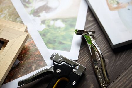 Photo canvas prints. Tools for wrapping.  Photographs, stretcher bars, staple gun and canvas pliers on brown wooden tableの写真素材