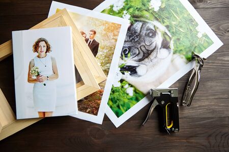 Photo canvas prints. Tools for wrapping.  Photographs, stretcher bars, staple gun and canvas pliers.  Printed photos of a dog and a wedding couple lying on a wooden table. Top viewの写真素材