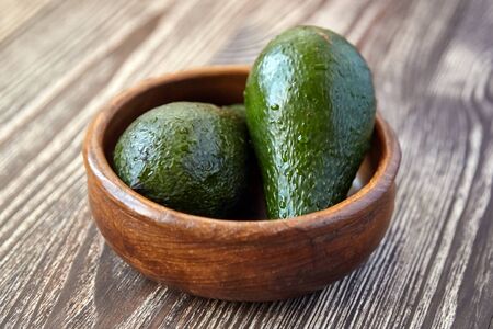 Avocados in a bowl on wooden background. Whole green fresh tropical fruits on brown tableの写真素材