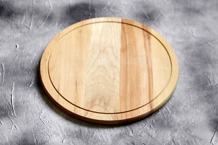 Empty round cutting board from beech wood on stone table, grey background, side viewの写真素材