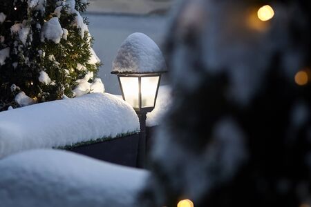 Glowing street lamp covered with snow, tree with electric light bulbs. Night light in the winter timeの写真素材