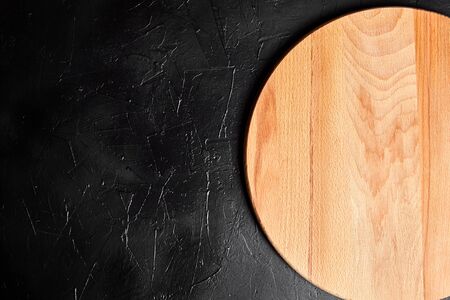 Cutting board on black stone table. Empty round beech wooden chopping board on dark background, top viewの写真素材