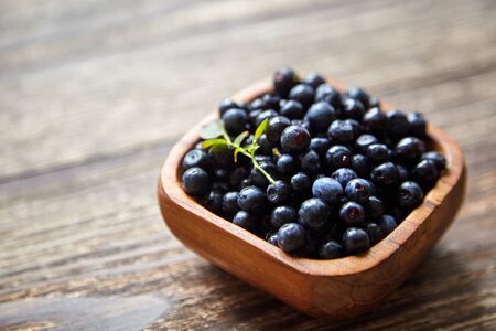 Bilberries with green leaves inside a bowl on brown wooden background. Fresh dark wild berries on tableの写真素材