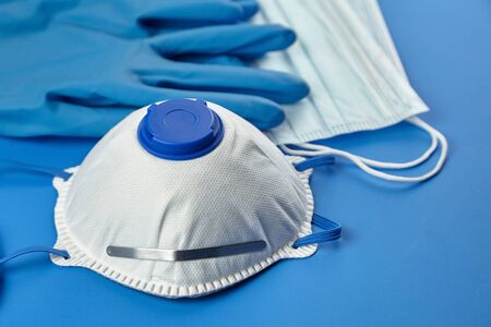 Respirator FFP2, disposable surgical face masks and rubber gloves on blue background. Protection against coronovirus COVID-19 pandemic. White filtering facepiece respirator n95, selective focusの写真素材