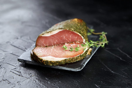 Jerky pork with spices, fresh green thyme, slate cutting board on black stone table. Polendwitz is a jerky tenderloin. Sun-dried filet, selective focusの写真素材