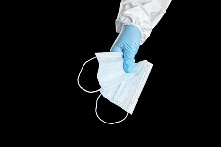 Face masks, disposable medical sanitary surgical masks in hand in blue glove, isolated on black...