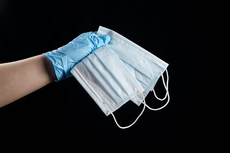 Person holding medical face masks, disposable sanitary surgical masks in hand in blue glove,...