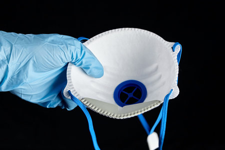 Filtering facepiece respirator in hand in blue glove, isolated on black background. N95 respirator....